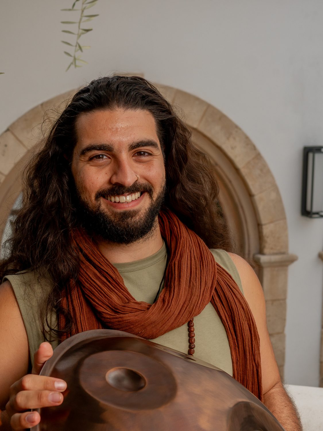 Emre Veçhi smiling, holding a copper VeChi Sound handpan in a sunny courtyard